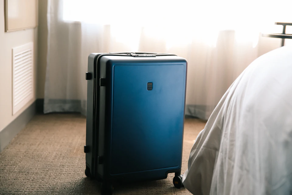 Blue suitcase on the floor beside a bed